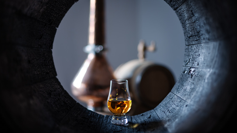 glass of bourbon in cask with still in background