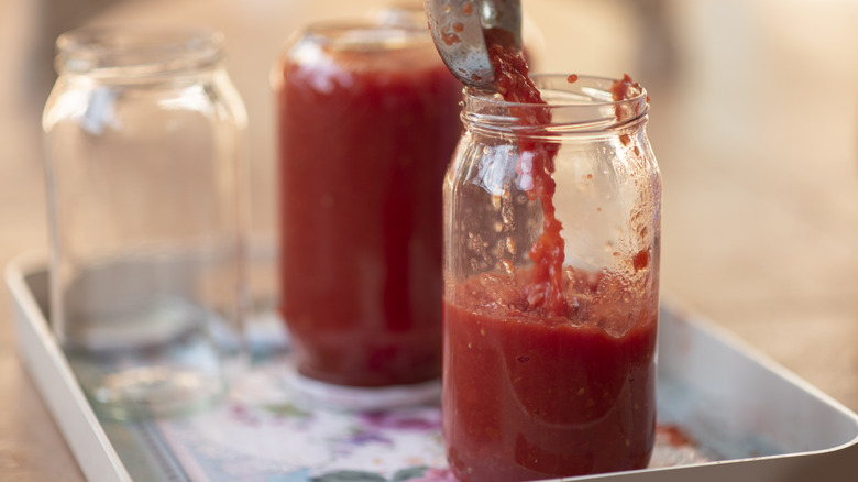 Spooning red sauce into jar