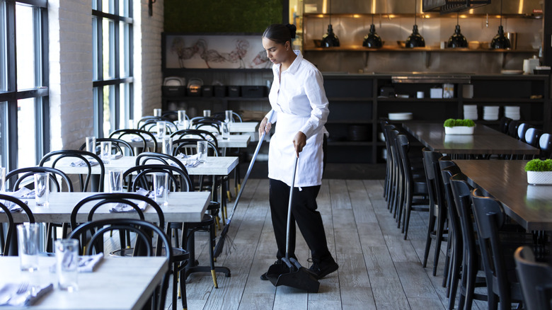 Woman busser sweeping restaurant floor