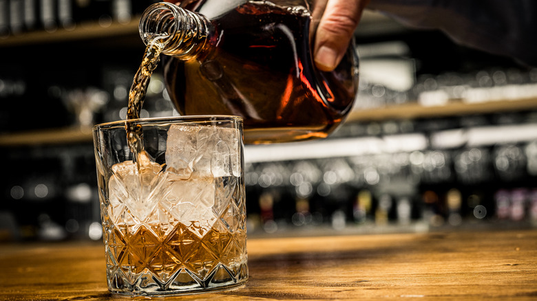 pouring bourbon into a cut glass tumbler over ice