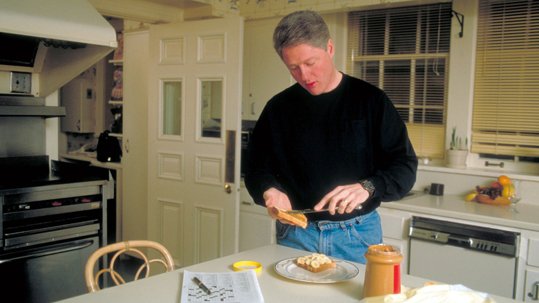 Bill Clinton makes himself a banana peanut butter sandwich and does the crossword in the kitchen