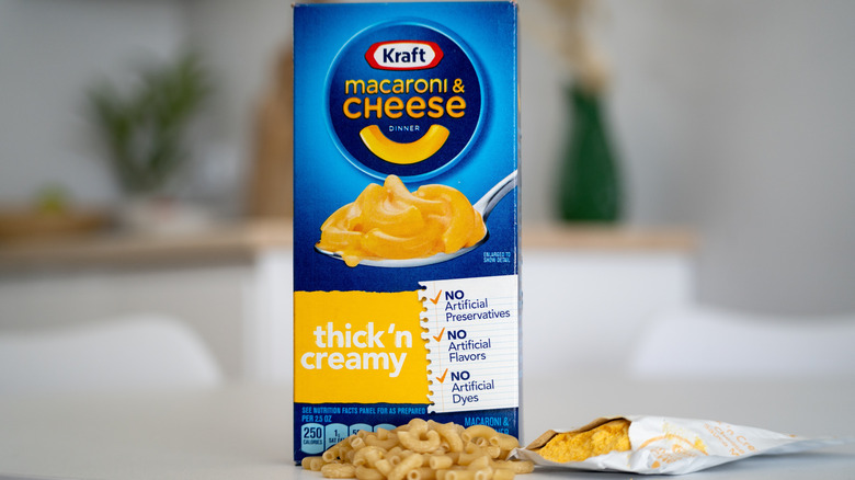 A blue box of Kraft macaroni and cheese sits on the countertop with macaroni noodles in front of the box and the powdered cheese sauce opened to the right of the box.