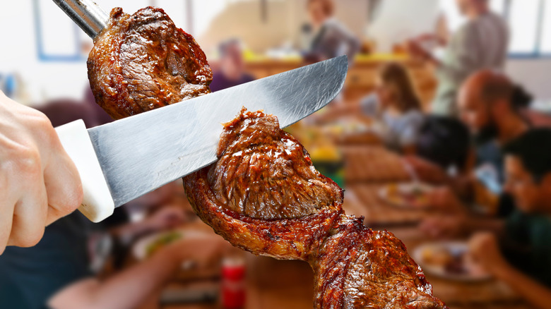 a large knife slicing into grilled meat on a metal skewer