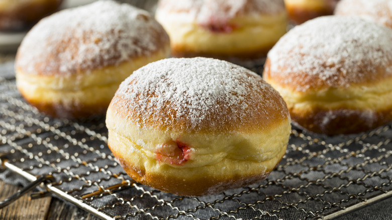 Powdered-sugar-topped jelly donuts sit on a cooling rack.