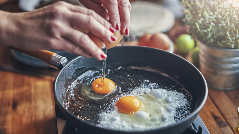 hands cracking an egg over a heated skillet