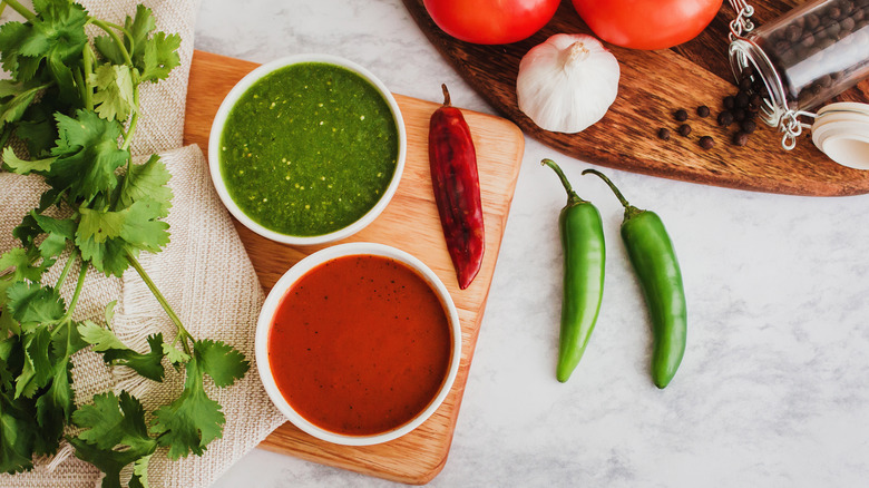 red and green salsa in serving dishes on a wood board