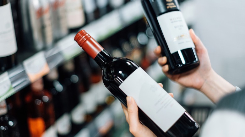 Hands holding two bottles of red wine in a store