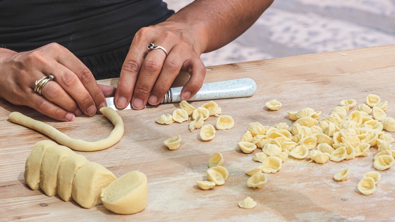 person shaping pasta dough with knife