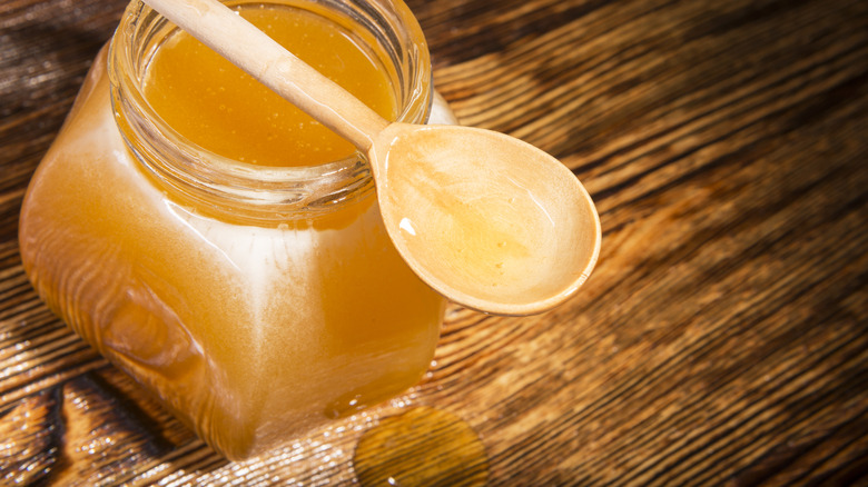 Glass jar of tupelo honey with a spoon against a wooden background