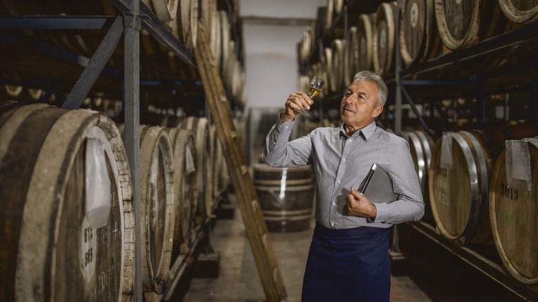 A man sampling whiskey from a barrel in a store room