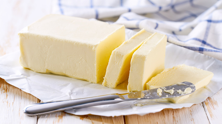 Sliced pieces of butter rest on a table beside a knife