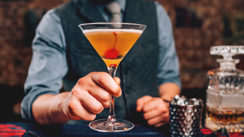 bartender passing cocktail garnished with cherry