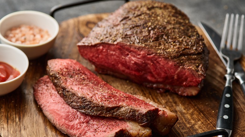 Roast beef slices on wooden slab with fork and knife