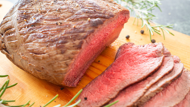 slices of roast beef on wooden slab with rosemary