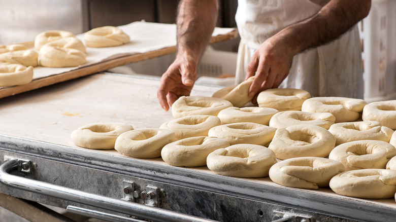 Hands placing raw donuts on baking sheet