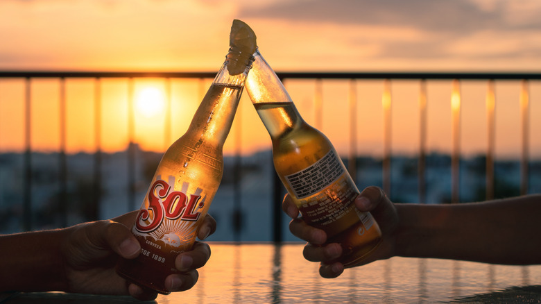 Clinking Sol bottles on balcony with a sunset in the background