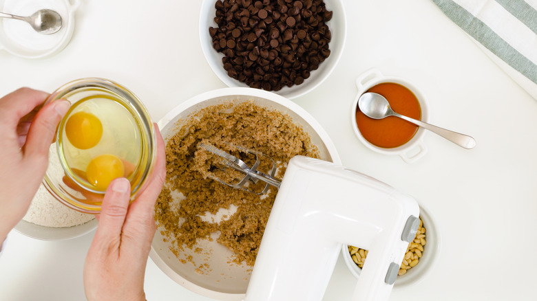 holding bowl of eggs over chocolate chip cookie dough