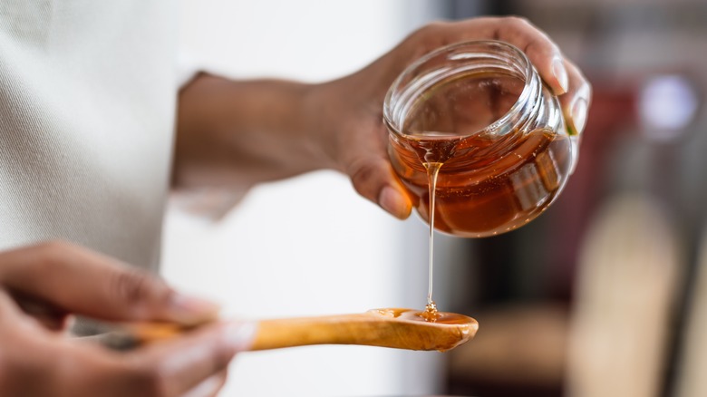 hands pouring honey onto spoon