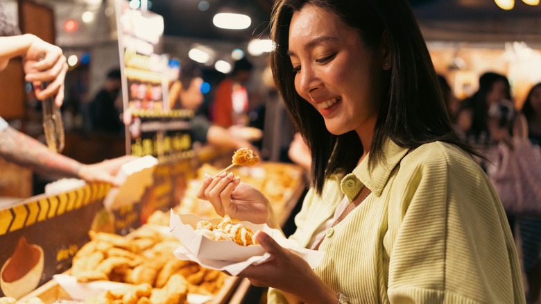 Woman smiling and sampling food at an Asian night market 