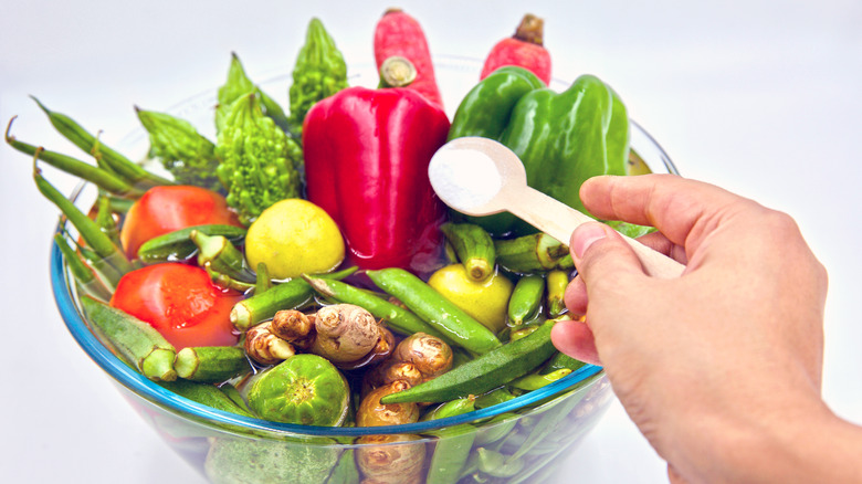 pouring cleaning powder on bowl of vegetables in water