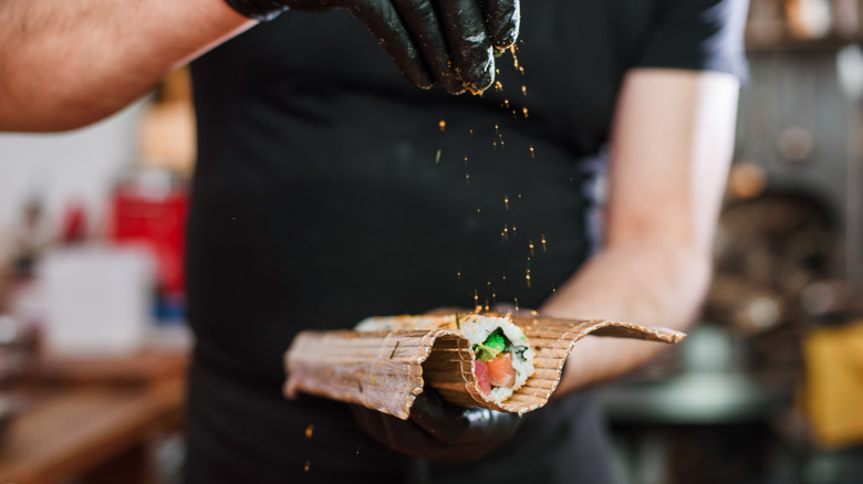 Sushi chef sprinkles togaroshi on a norimaki roll