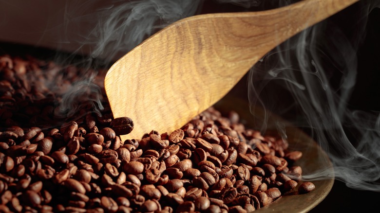 Smoky roasted coffee beans in a pan with wooden spoon