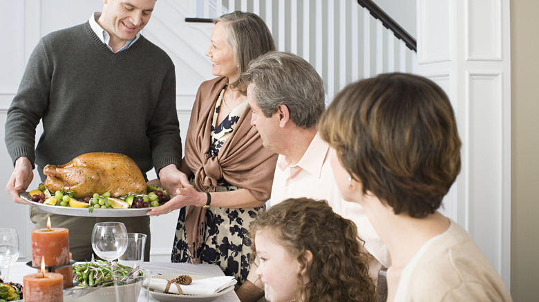 man serving thanksgiving turkey to family table