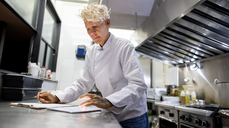 A chef working on a menu or shopping list in a professional kitchen