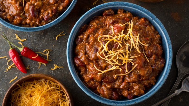 Top-down view of a bowl of chili next to red peppers