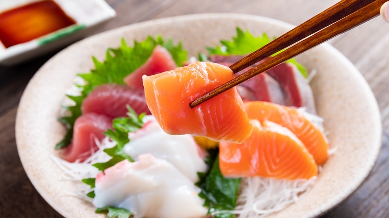 Chopsticks holding a piece of sashimi over a platter