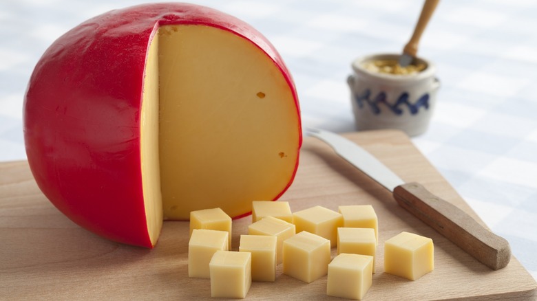 Round wheel of Edam in red wax with cubes on a wooden board