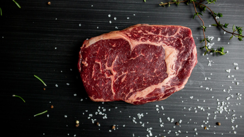 Ribeye steak with coarse salt and herbs against a dark background