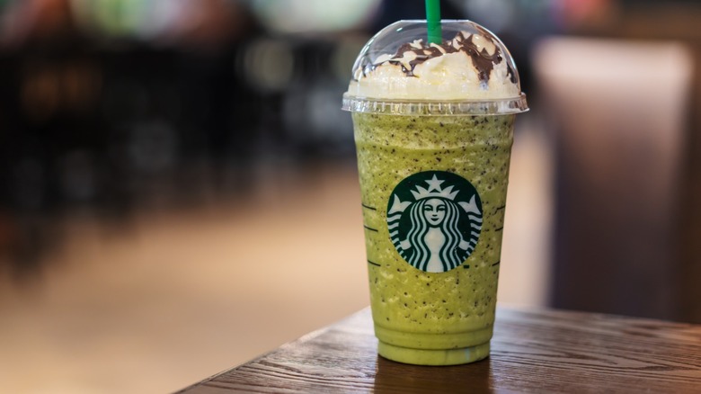 A green Starbucks blended drink with whipped cream on a wooden counter