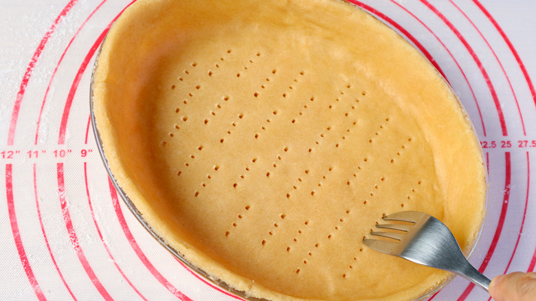 A pie crust being docked by a fork