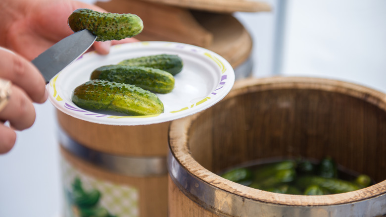 pickles on a paper plate with a pickle barrel in the background