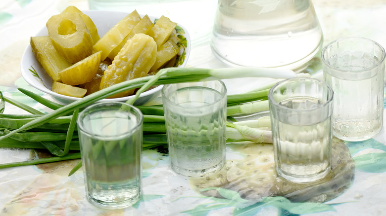 sliced pickles on a table with shots of vodka