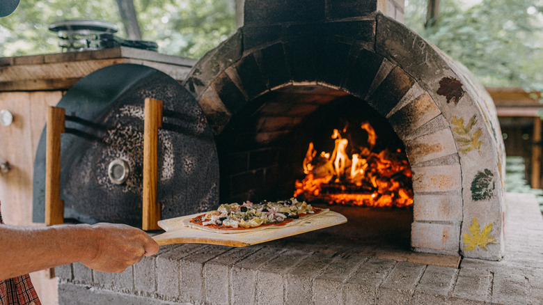 A person using a wooden pizza peel to place a pizza in a brick oven