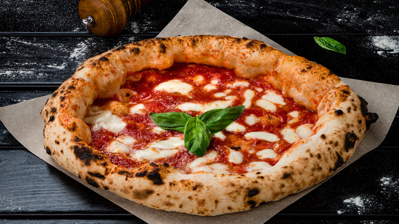 Neapolitan pizza sits on a wooden table surrounded by flour