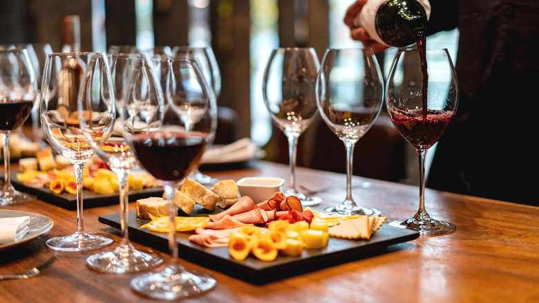 A person pouring wine for a home wine-tasting at a table full of charcuterie