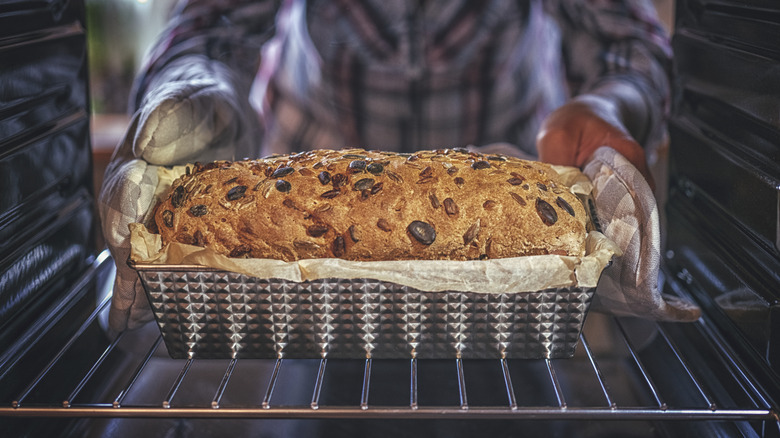 Home cook pulling a loaf of bread in a metal pan out of the oven