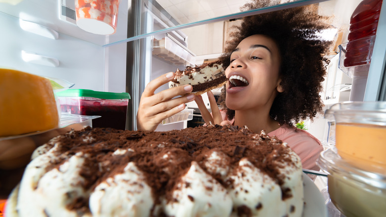 Woman eating cake from fridge