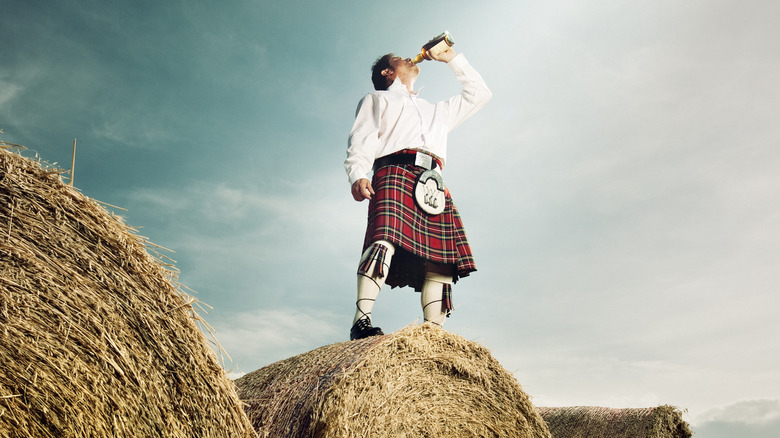 Man in kilt drinking whiskey on hay bale