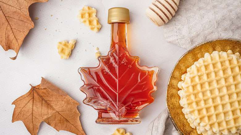 A leaf-shaped bottle of maple syrup beside a stroopwafel and some leaves