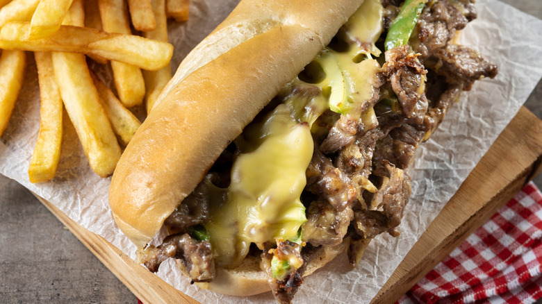 Philly cheesesteak on wood board with french fries