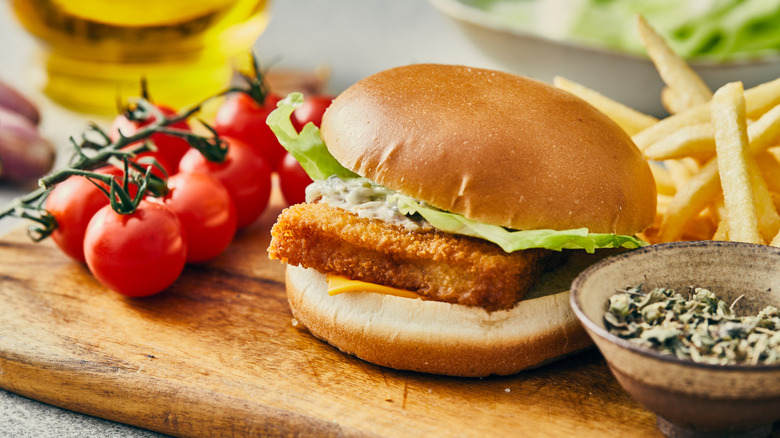 fish sandwich with lettucce, mayo, and cheese with fries and tomatoes