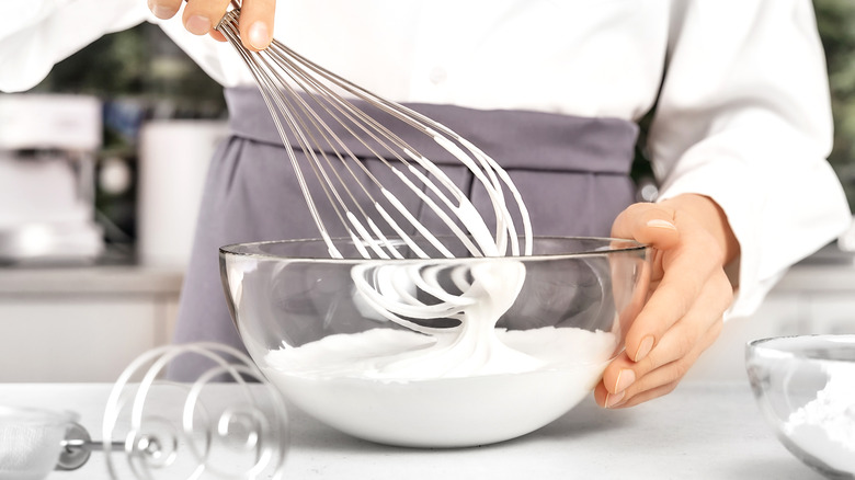 Hand holding whisk in bowl of whipped cream