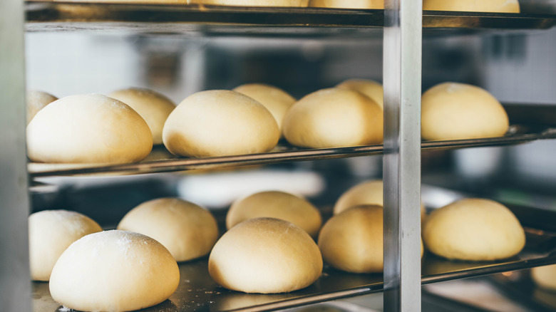 two rows of buns ready for the oven sitting on an industrial baking rack