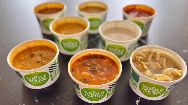 Various Whole Foods soups in containers assembled on a dark countertop
