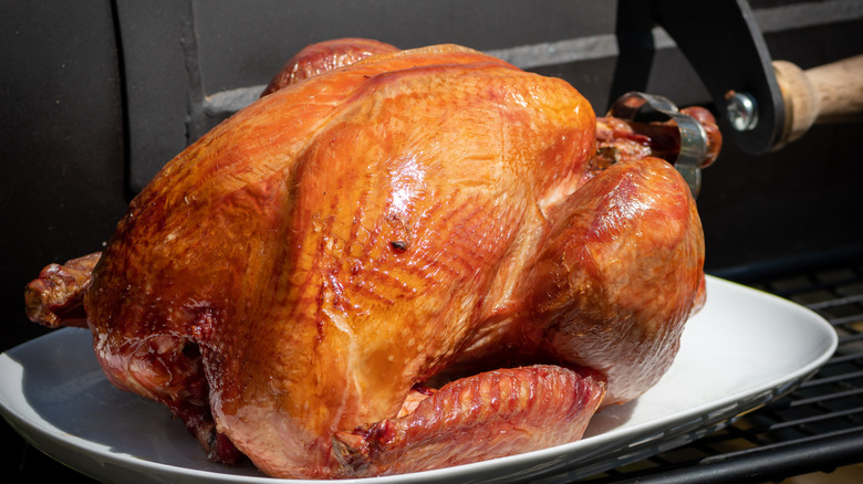 whole smoked turkey fresh out of the smoker sitting on a white platter