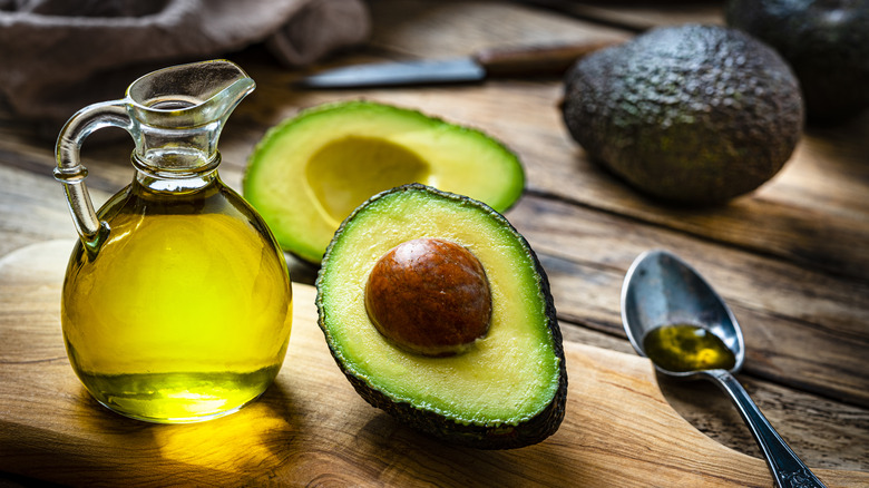 avocado oil with two avocado halves on a wood cutting board